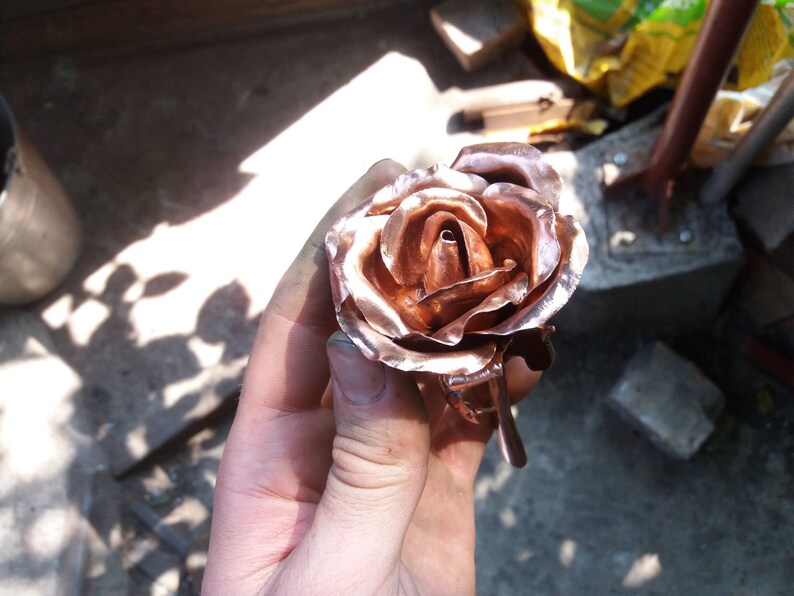 May include: A copper rose sculpture with a detailed, realistic design. The rose is crafted with intricate petals and a delicate stem.