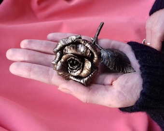 May include: A gold-colored metal rose with a detailed stem and leaves. The rose is held in a person's hand.