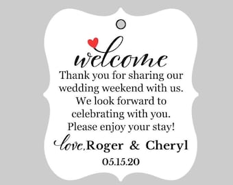 May include: White wedding welcome tag with a red heart and the text "welcome" in a decorative font. The tag also includes the text "Thank you for sharing our wedding weekend with us. We look forward to celebrating with you. Please enjoy your stay! love, Roger & Cheryl 05.15.20"