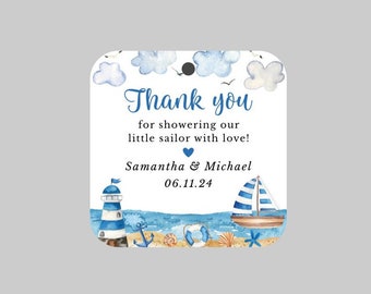 Può includere: Etichetta di ringraziamento a tema nautico blu e bianco con un faro, una barca a vela, un'ancora e conchiglie. Il testo recita "Grazie per aver coccolato il nostro piccolo marinaio con amore! Samantha & Michael 06.11.24"