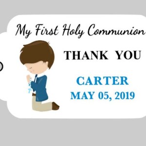 Puede incluir: Una etiqueta de agradecimiento blanca con una ilustraci&oacute;n de dibujos animados de un ni&ntilde;o con un traje azul arrodillado en oraci&oacute;n. La etiqueta dice "My First Holy Communion" y "Thank You" con el nombre del ni&ntilde;o "Carter" y la fecha "May 05, 2019" impresa debajo.