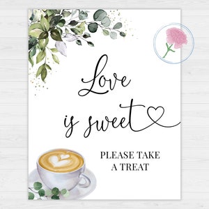 Op de afbeelding: Een wit bord met groen gebladerte en gouden glitter aan de randen. Het bord zegt "Love is sweet" met een hartje. Onder de tekst is een aquarel-illustratie van een kopje koffie met een hartvormig ontwerp in het schuim. Het bord zegt ook "Please take a treat".