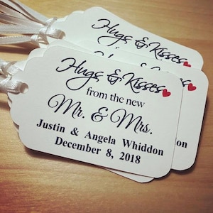 May include: White wedding favour tags with black calligraphy that reads "Hugs & Kisses from the new Mr. & Mrs." with the couple's names, "Justin & Angela Whiddon", and wedding date, "December 8, 2018".