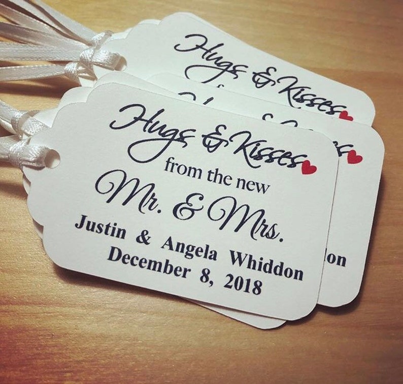 May include: White wedding favour tags with black calligraphy that reads "Hugs & Kisses from the new Mr. & Mrs." with the couple's names, "Justin & Angela Whiddon", and wedding date, "December 8, 2018".