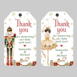 May include: Two white gift tags with gold snowflakes and a gold glitter background. One tag features a watercolor illustration of a Nutcracker soldier and the text "Thank you for showering our baby with love! Samantha & Michael". The other tag features a watercolor illustration of a ballerina and the text "Thank you for showering our baby with love! Samantha & Michael".