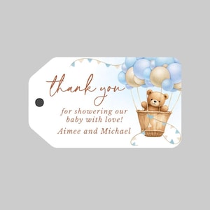 May include: Thank you for showering our baby with love! Aimee and Michael. A white tag with brown text and a blue and beige hot air balloon with a teddy bear inside.