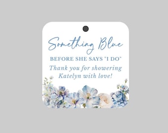 May include: A white tag with rounded corners and a black hole at the top. The tag features the text "Something Blue" and "Before She Says 'I Do'". Floral watercolor art in shades of blue and white adorns the bottom.