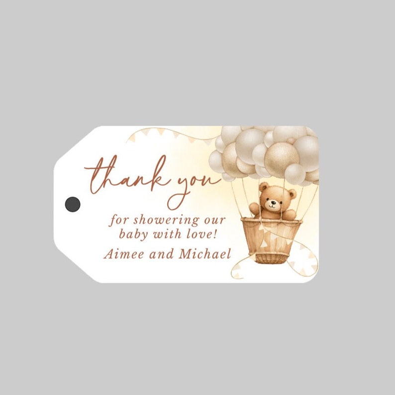 May include: Thank you for showering our baby with love! Aimee and Michael. A brown teddy bear sits in a hot air balloon with white and beige balloons. The balloon is surrounded by a yellow and white background with white bunting.