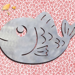 Może przedstawiać: Srebrny metalowy wycinany kształt ryby ze stylizowanym wzorem. Ryba znajduje się na czerwono-białym tle z kwiatami.