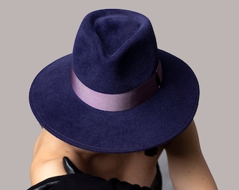 May include: A dark blue fedora hat with a purple ribbon band. The hat is made of felt and has a wide brim.