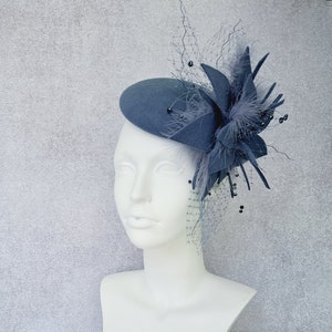 May include: A gray felt hat with a large gray flower and black beads. The hat is on a white mannequin head.
