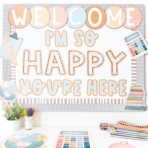 May include: A classroom bulletin board with the words "WELCOME I'M SO HAPPY YOU'RE HERE" in a playful font. The board is decorated with school-themed elements like a calculator, books, and a globe, creating a welcoming atmosphere.