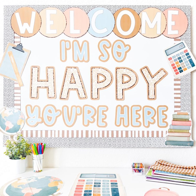 May include: A classroom bulletin board with the words "WELCOME I'M SO HAPPY YOU'RE HERE" in a playful font. The board is decorated with school-themed elements like a calculator, books, and a globe, creating a welcoming atmosphere.