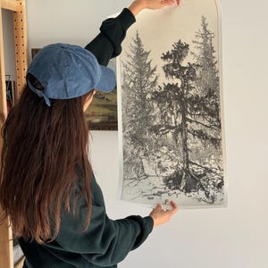 May include: A black and white print of a forest scene with tall trees. The print is on a white background and is being held by a person.