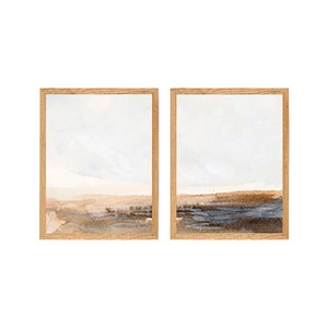 May include: A set of two framed watercolor paintings depicting abstract landscapes with muted tones of blue, brown, and beige.