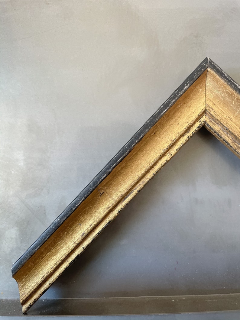 Puede incluir: Primer plano de una esquina de un marco de imagen con acabado negro y dorado. El marco tiene un borde elevado y un dise&ntilde;o decorativo.