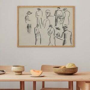 Op de afbeelding: Een ingelijste zwart-wit schets van een groep mensen met hoeden. De schets hangt aan een witte muur boven een houten tafel met een kom fruit en een bord met een plak meloen.