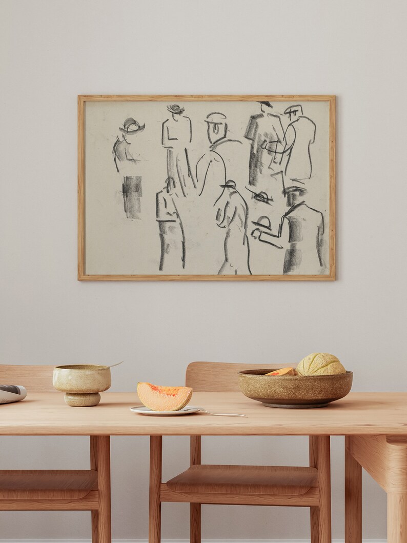Op de afbeelding: Een ingelijste zwart-wit schets van een groep mensen met hoeden. De schets hangt aan een witte muur boven een houten tafel met een kom fruit en een bord met een plak meloen.