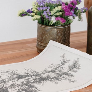 May include: A white sheet of paper with a detailed black and white drawing of a tree branch. The paper is lying on a wooden table next to a vase of purple, white, and yellow flowers.