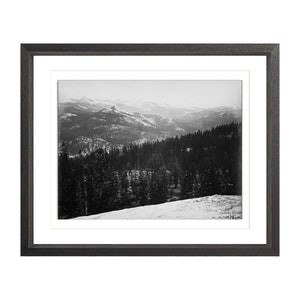 May include: A black and white photograph of a snowy mountain range with a forest in the foreground.