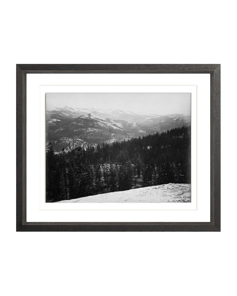 May include: A black and white photograph of a snowy mountain range with a forest in the foreground.