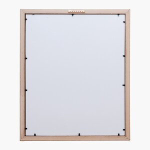 Puede incluir: Un marco de fotos de madera marr&oacute;n claro con un paspart&uacute; blanco y un peque&ntilde;o gancho de colgar dorado en la parte superior. El marco est&aacute; listo para colgar.