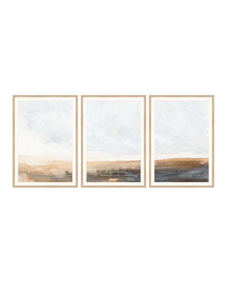 K&ouml;nnte beinhalten: Ein Set aus drei gerahmten Aquarellbildern, die abstrakte Landschaften in gedeckten Blaut&ouml;nen, Braun- und Beiget&ouml;nen darstellen.