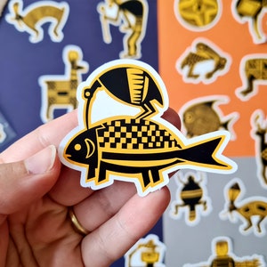 May include: A black and yellow sticker of a stylized fish with a bird perched on top. The fish has a checkered pattern and the bird has a rounded body and a long beak.