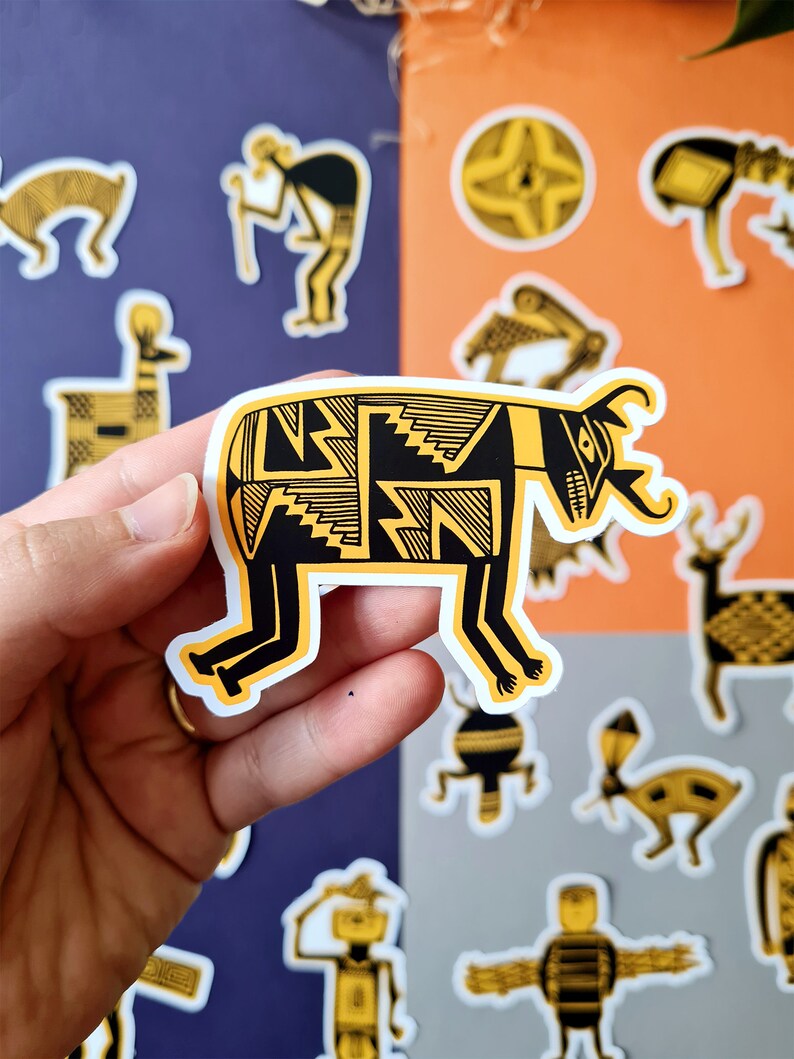 May include: A black and yellow patterned sticker of a stylized animal with a long snout and horns. The sticker is on a white background and is being held by a hand.