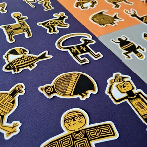 May include: A set of 14 black and gold stickers featuring various animal and human figures. The stickers are on a purple background. The stickers are all in a stylized, geometric style.