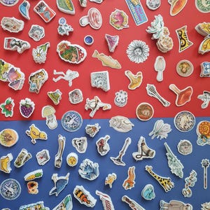 Puede incluir: Una colección de pegatinas coloridas con varios diseños, incluyendo flores, animales y formas abstractas, dispuestas sobre un fondo rojo y azul. Algunas pegatinas presentan texto, como "STEMBOLTS" y "OBEY". Las pegatinas son de varios tamaños y formas.