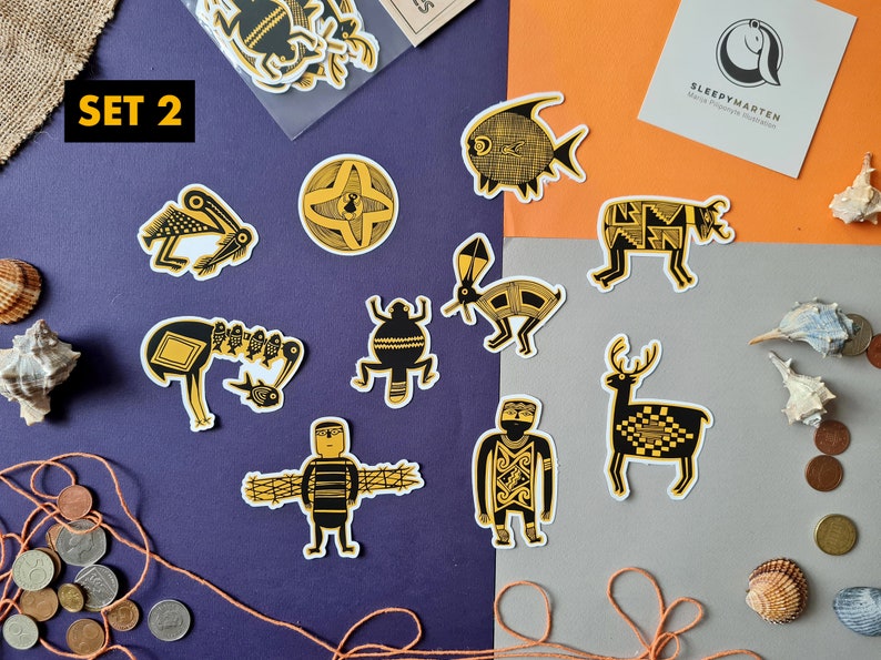 May include: Set of 10 black and gold patterned stickers featuring various animal and geometric designs. The stickers are on a purple and gray background with a small piece of burlap fabric and some seashells.