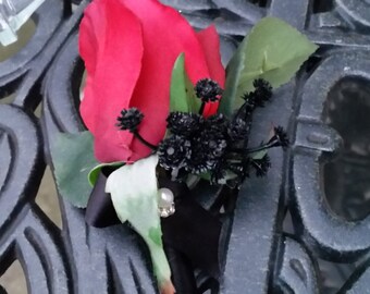 Real touch Red rose bud with black baby's breath. Wrapped in black satin and accented with a pearl and rhinestone pin.