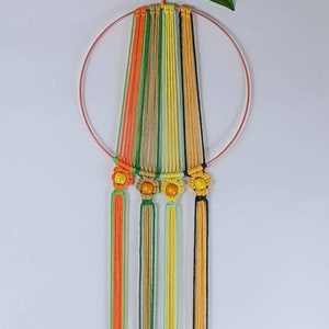 May include: A macrame wall hanging with a circular wooden hoop and colourful yarn strands. The strands are tied with small orange and yellow beads to create a flower design.