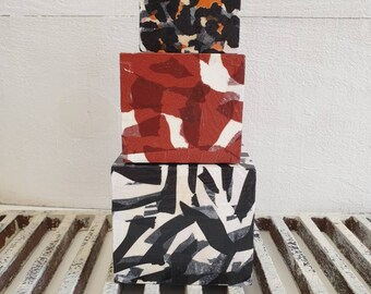 May include: Three stacked square blocks with abstract patterns. The top block has a black, orange, and gray animal print. The middle block features a red and white design. The bottom block displays a black and white abstract pattern.