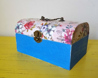 May include: A small wooden box with a blue base and a floral patterned lid. The lid has a metal latch and a handle.