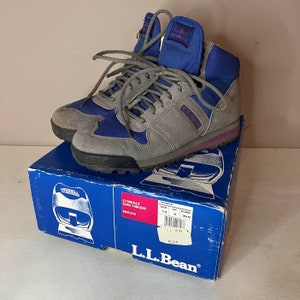 May include: Gray and blue suede hiking boots with a purple trim. The boots are on a blue box with the text "Cobalt Day Hiker M629" and "L.L.Bean" printed on it. The box also shows the size of the boots in US, UK, and Euro sizes.
