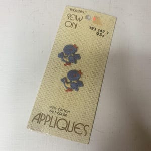 May include: Two small blue bird embroidered sew-on appliques on a beige cardboard backing card. The card features the text Wrights SEW ON 193 147 2 95 cents 100% COTTON FAST COLOR APPLIQUES. The birds have orange beaks and feet with blue wings.