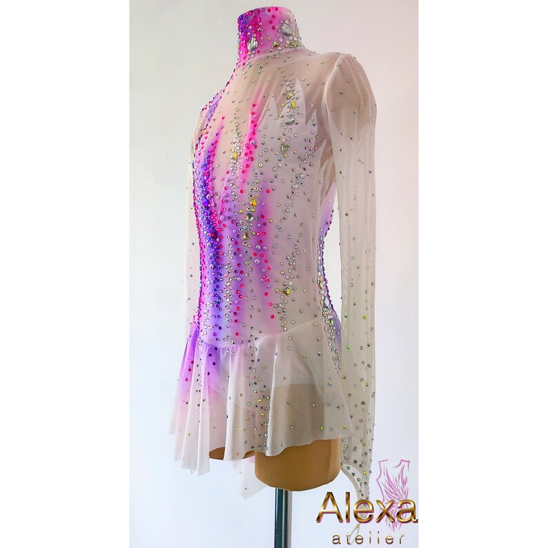 May include: White figure skating dress with long sleeves and a high neck. The dress has a pink and purple ombre design with rhinestones.