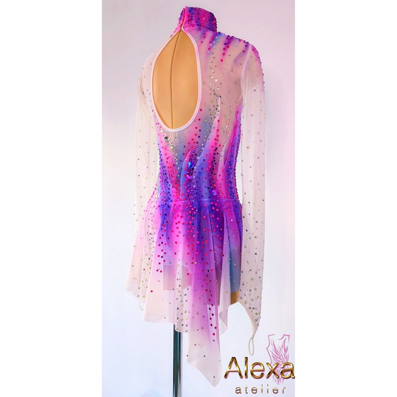 May include: A white, long-sleeved figure skating dress with a pink and purple ombre design and rhinestones. The dress has a keyhole back and a short, asymmetrical skirt.