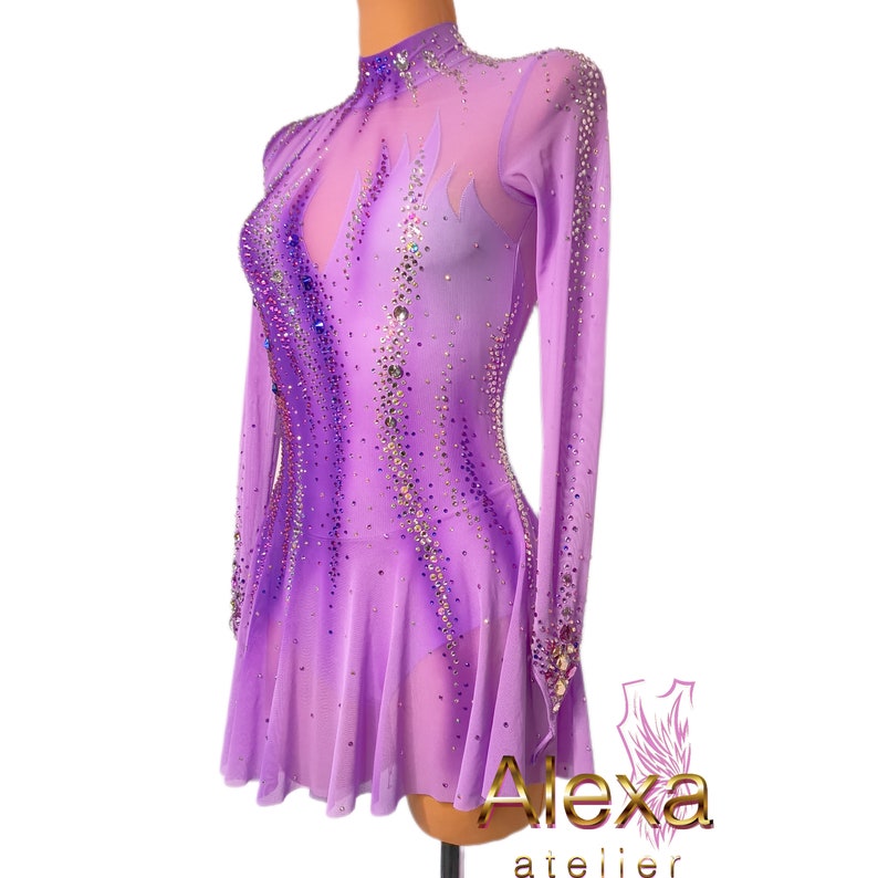Pu&ograve; includere: Un abito da pattinaggio artistico viola con un'overlay trasparente e un design a fiamma. L'abito &egrave; decorato con strass e ha maniche lunghe.