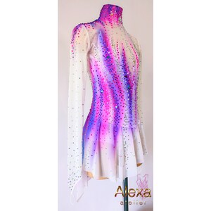 May include: A white figure skating dress with long sleeves and a high neck. The dress has a purple and pink ombre design with rhinestones throughout. The dress has a short skirt with a ruffled hem.