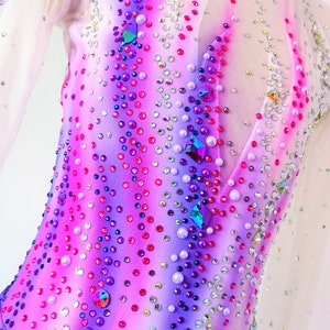 May include: A white, pink, and purple figure skating dress with a sheer bodice and a ruffled skirt. The dress is covered in rhinestones and crystals.