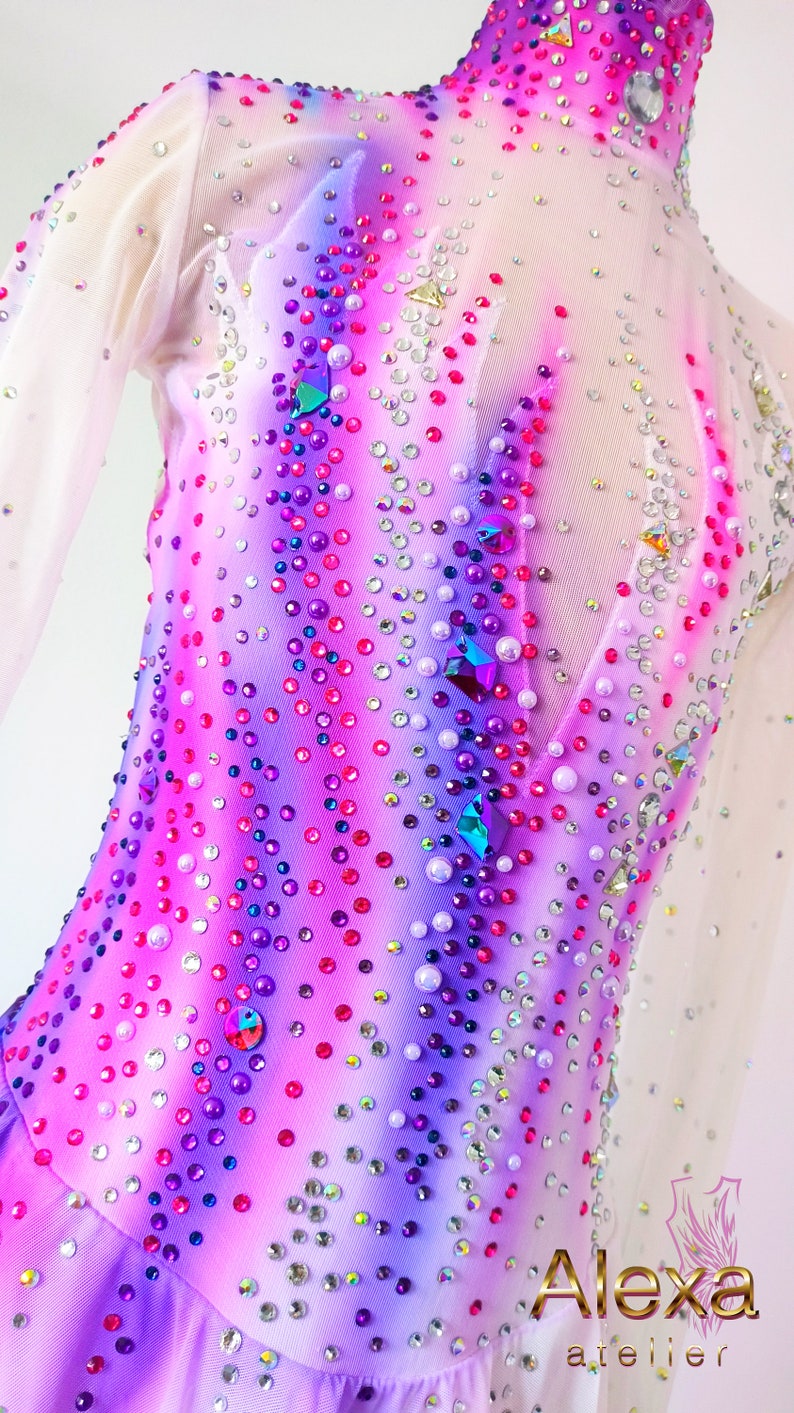 May include: A white, pink, and purple figure skating dress with a sheer bodice and a ruffled skirt. The dress is covered in rhinestones and crystals.