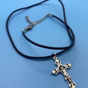 Peut inclure: Un collier en cordon noir avec un pendentif crucifix argenté. Le pendentif représente la figure de Jésus sur la croix avec les lettres INRI inscrites en haut. Le collier comprend un fermoir mousqueton en métal argenté et une chaînette réglable.
