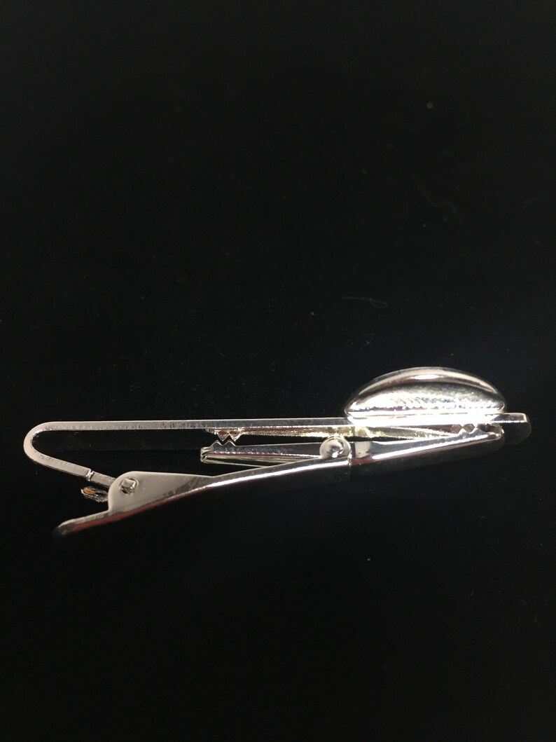 May include: Silver tie clip with a rounded, textured top. The clip is designed to hold a tie in place.