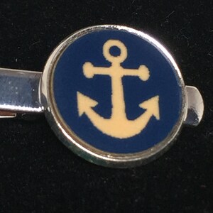 May include: A silver tie clip with a round blue enamel charm featuring a yellow anchor.