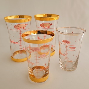 May include: Four vintage drinking glasses with gold rims. Each clear glass has a pink pig illustration, red measurement markings, and the words "Gentlemen" and "Ladies".