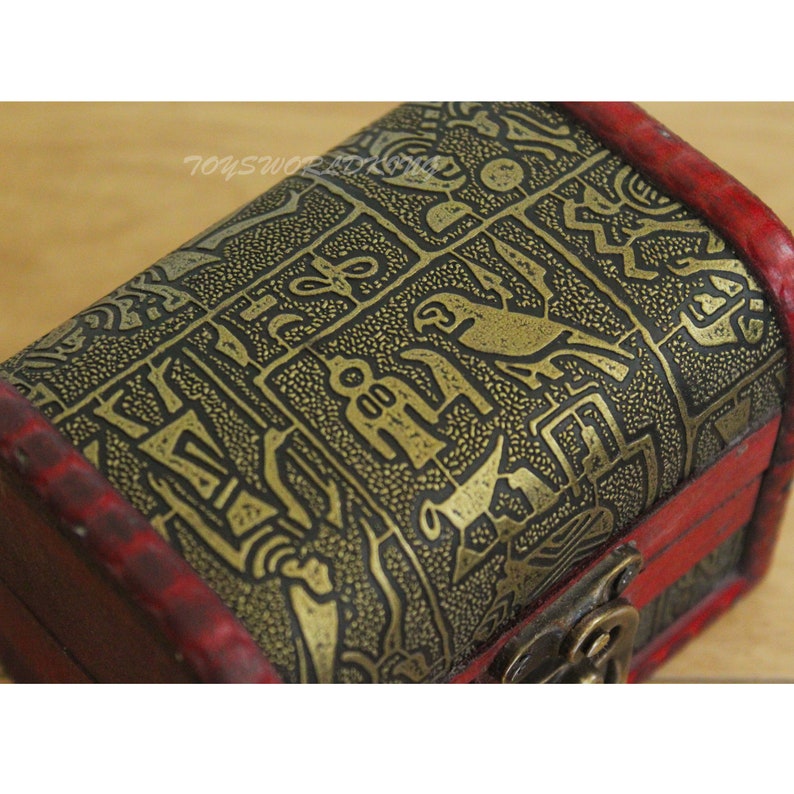 May include: A small wooden treasure chest with a red lid and gold patterned design. The chest has a metal latch and hinges.