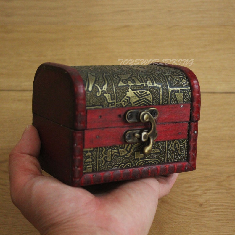 May include: A small wooden treasure chest with a red and gold finish. The chest has a decorative pattern and a brass latch.